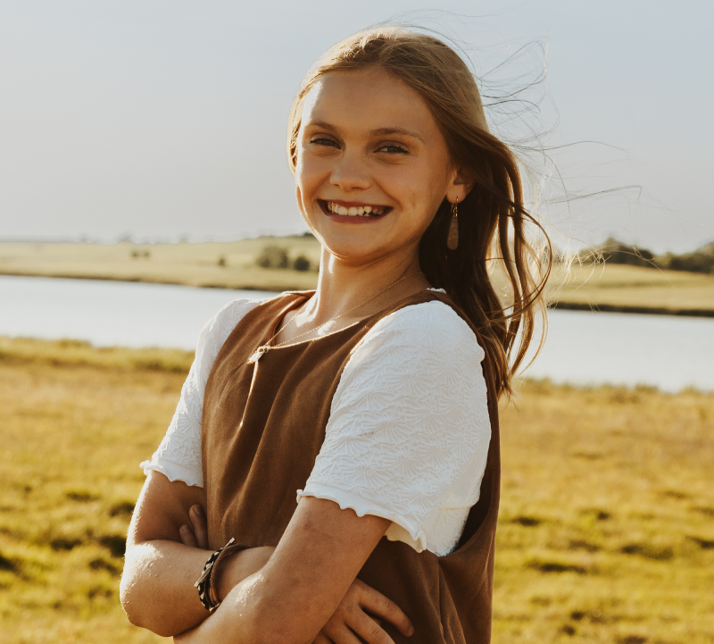 Black and white photo of young girl in short sleeve blouse standing in a pasture