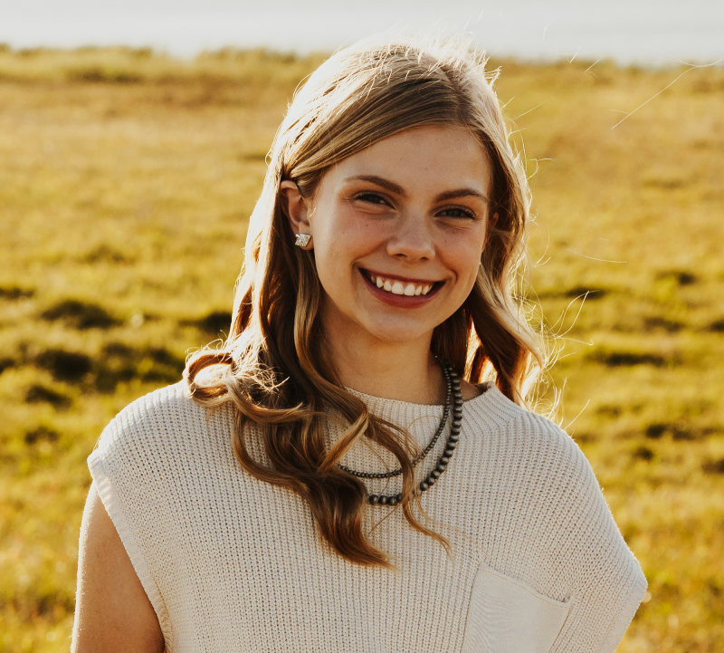 Young girl with long blonde hair and white blouse standing in a pasture