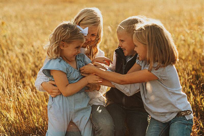 Photo of three young girls and one boy sitting in a pasture tickling each other and laughing